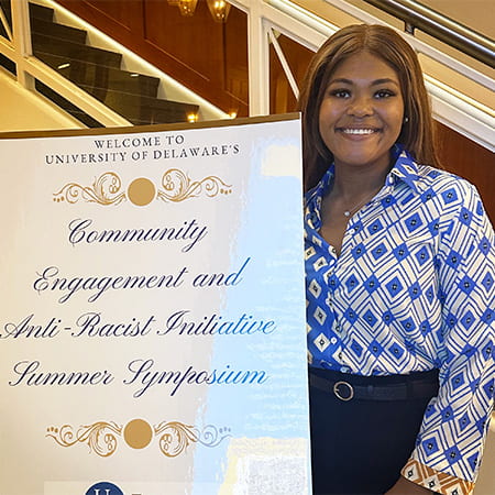 Chelsia Douglas stands beside the summer grad symposium poster
